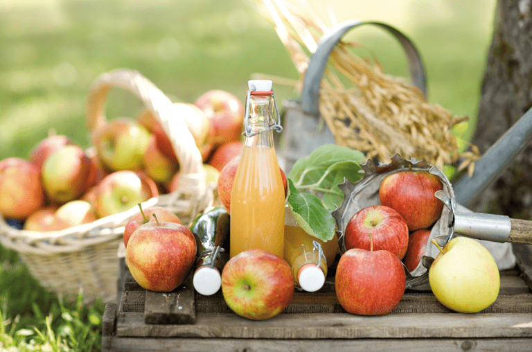 Tisch mit frischen Äpfeln, Apfelsaft und Pflücker vor Korb mit Äpfeln
